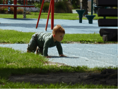 A child crawling on soft matting in a playground.