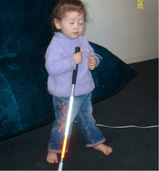 A young child holding the top of a cane, tapping the cane on the floor.