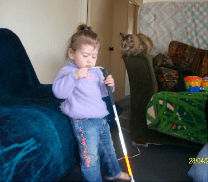A young child leaning against a sofa exploring the handle of a cane.