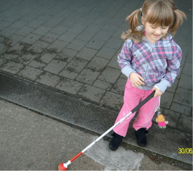 A young girl standing outside holding her cane.