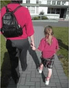Adult and child walking along a path. The adult is guiding the child. The child is holding onto the adults fingers as she is not tall enough to take the adults wrist.