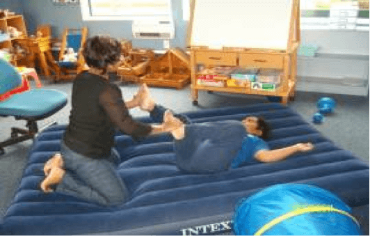 An adult holding a childs legs on an airbed helping the child to sense movement of their body.
