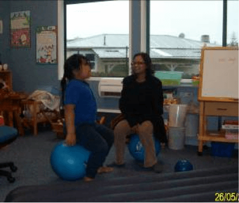 Child and teacher aide in a classroom, bouncing on fitness balls.