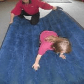 Child crawling on an airbed while the O & M instructor holds and moves the airbed around.