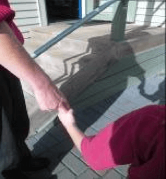 Child is holding on to adult's fingers, steps in the background.