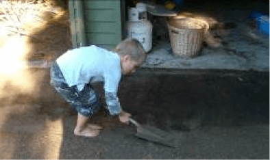 Child with a spade cleaning up sand outside a building.