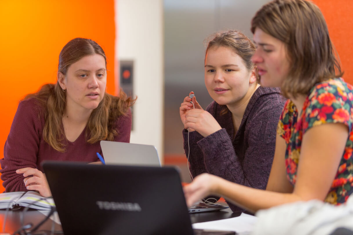 Mary sitting with two peers at a table in front of a laptop.