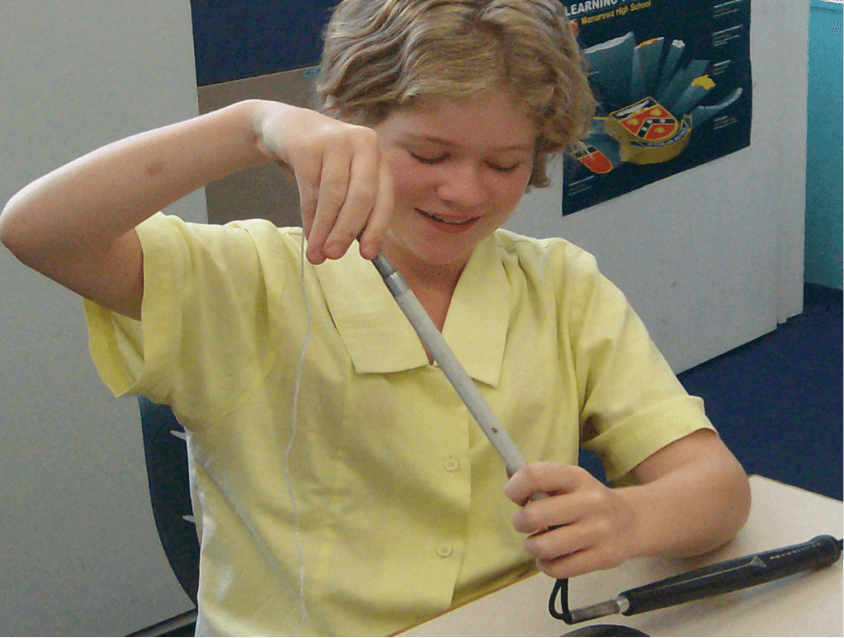 Jesse has replaced the broken part of the cane with a new bit and is re threading her cane using the string knotted onto the elastic and the paper clip to weight the string through the pieces of cane.