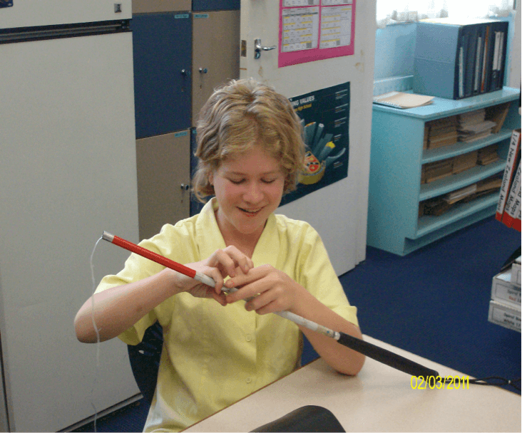 Jesse his sitting at a table holding her cane and has the string attached to the elastic poking out of the very end.