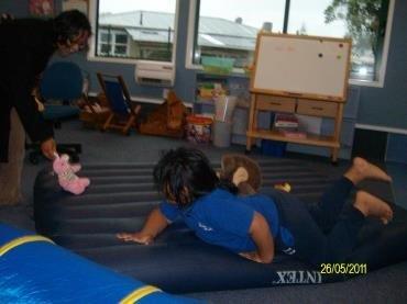 Learner is crawling on an airbed in a classroom to develop motor and vision skills.