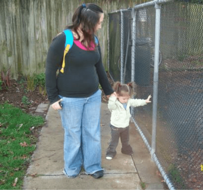Mum with her toddler walking along a fence. Mum is guiding toddler, toddler is trailing hand along the fence.