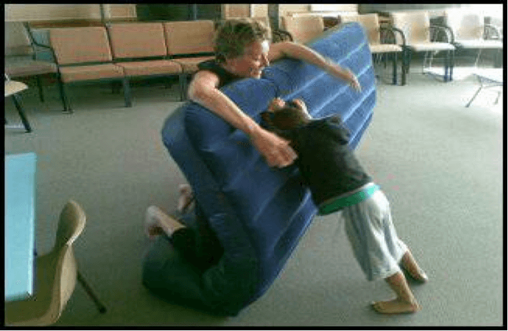 O & M instructor holding up an airbed while child pushes against the airbed from the other side.
