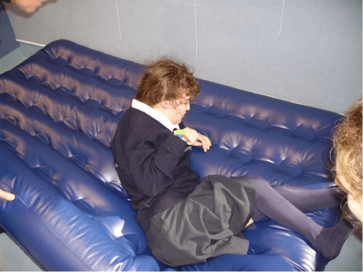 Sam is leaning on her left elbow and the O & M Instructor is lifting the corner of the airbed.