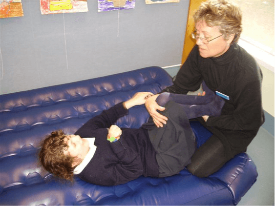 Sam is lying on the airbed with her legs bent up at a 90 degree angle, the O & M Specialist is holding Sam's legs against her stomach.