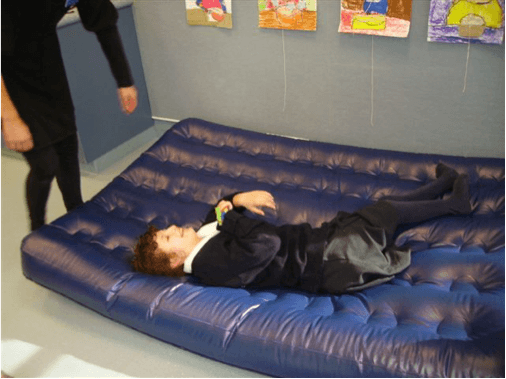 Samantha, a student who normally uses a wheelchair and is blind, is laying on the airbed smiling.