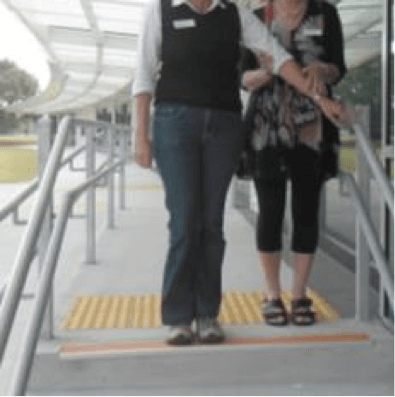 Sighted guide and person who has a vision impairment standing at the top of the steps, guide's left arm touching hand rail.