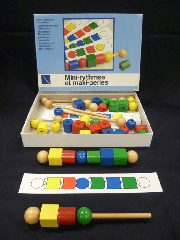 A box of large coloured wooden shape beads with dowel to thread them on.