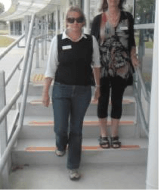 The guide reaches the bottom step and the person with vision impairment is on the previous step.