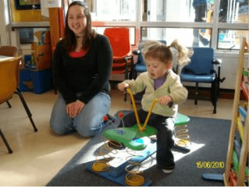 Toddler child sitting on a bouncy spring caterpillar toy with mum sitting to her right.