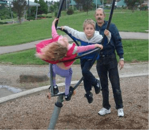 Two children on a rotating peice of playground equipment being watched by an adult.