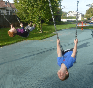 Two children on swings in a playground leaning their bodies back.