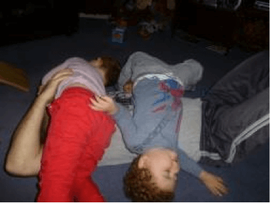 Two children rolling on top of their dad, rough and tumbling.