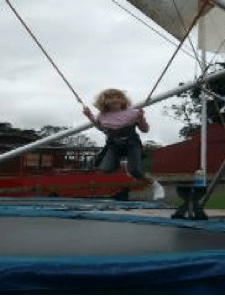 Young girl in mid air, attached to a bungy, above a trampoline.