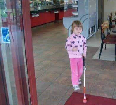 Young learner using her cane to visit in a cafe entrance.