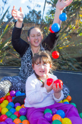 Giana and her mum sit on the trampoline with coloured plastic balls