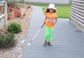 A young learner is walking confidently using her cane to follow the garden edge