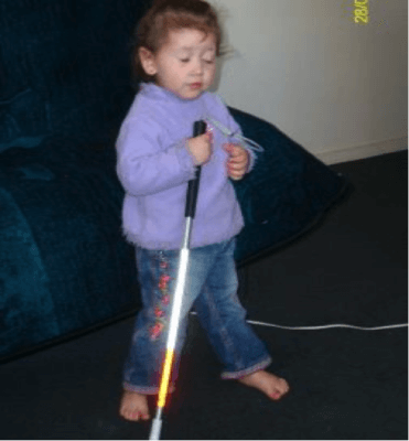 A young child holding the top of a cane, tapping the cane on the floor