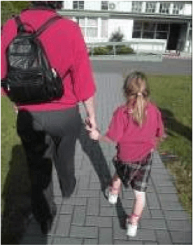 Adult and child walking along a path. The adult is guiding the child. The child is holding onto the adults fingers as she is not tall enough to take the adults wrist