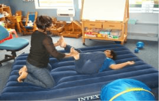 An adult holding a childs legs on an airbed helping the child to sense movement of their body