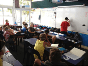 Brayden at the front writing on the whiteboard, students sit watching from their desks