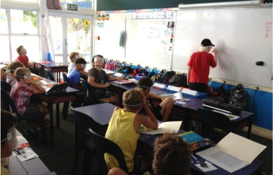 Brayden at the front writing on the whiteboard, students sit watching from their desks