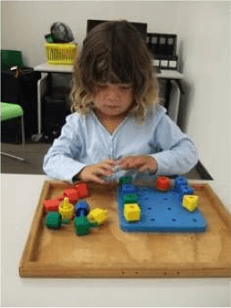 Charlotte sits at a table completing a pegboard activity