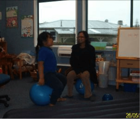 Child and teacher aide in a classroom, bouncing on fitness balls