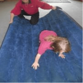 Child crawling on an airbed while the O & M instructor holds and moves the airbed around