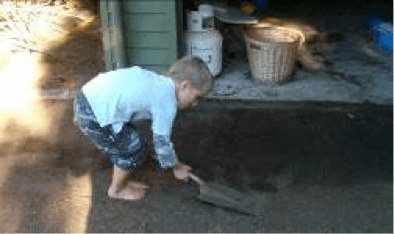 Child with a spade cleaning up sand outside a building