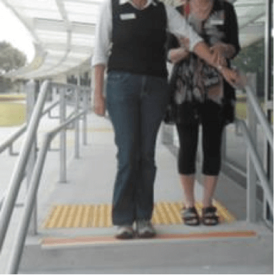 Sighted guide and person who has a vision impairment standing at the top of the steps, guide's left arm touching hand rail