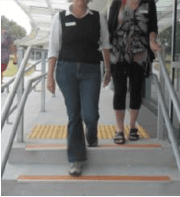 Sighted guide stepping down the first step down and person with vision impairment is standing at the top of the steps