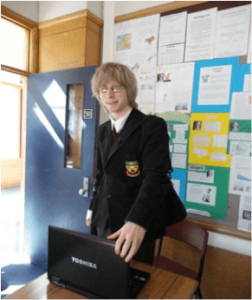 Student standing in front of desk with laptop on it