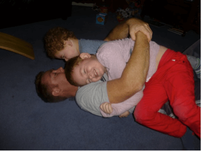 Two children laying on top of their dad on the floor playing, rough and tumble