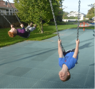 Two children on swings in a playground leaning their bodies back