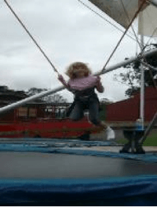 Young girl in mid air, attached to a bungy, above a trampoline