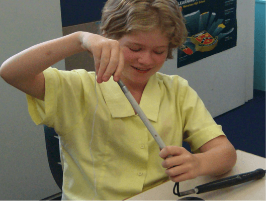 Jesse has replaced the broken part of the cane with a new bit and is re threading her cane using the string knotted onto the elastic and the paper clip to weight the string through the pieces of cane