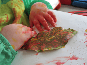 Child’s hands using fingerpaint on a large leaf