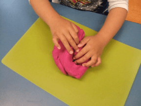 Child’s hands exploring a lump of pink playdough