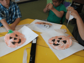 Three children tearing strips of paper to stuff into pumpkin shapes