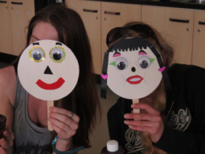 Two people sitting holding face plates in front of their faces